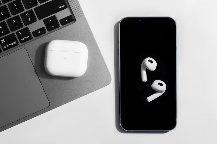 White wireless earbuds case next to a phone on a laptop